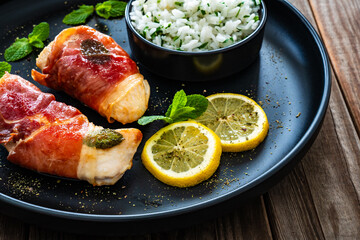 Chicken Saltimbocca - pan-fried chicken cutlets wrapped in Italian prosciutto slices on wooden table	
