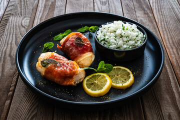 Chicken Saltimbocca - pan-fried chicken cutlets wrapped in Italian prosciutto slices on wooden table	
