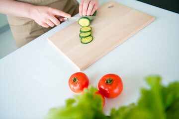 Young woman with red hair slicing cucumber in kitchen for a healthy meal preparation on a casual daylight day