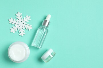 Winter skin care concept. Cosmetic products packaging design. Dropper bottle with serum, moisturizer cream jar and snowflakes on color background. Flat lay, top view.