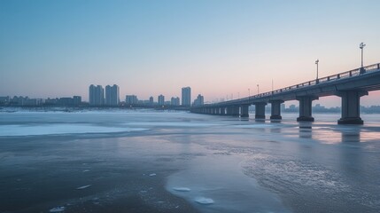 Obraz premium City skyline at sunrise over a frozen river with bridge.