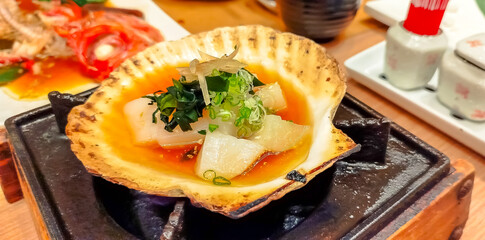 Hotate, Japanese style scallop, grilled with its shell with sake (Japanese alcohol spirit), on table top fire hearth in Japanese style restaurant