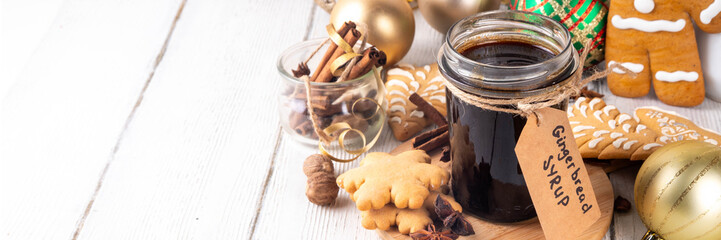 Homemade gingerbread syrup in jar, Christmas cookies and cake, drinks and cocktails ingredient with honey, sugar, spices, on kitchen table with gingerbread cookies and Christmas decorations 