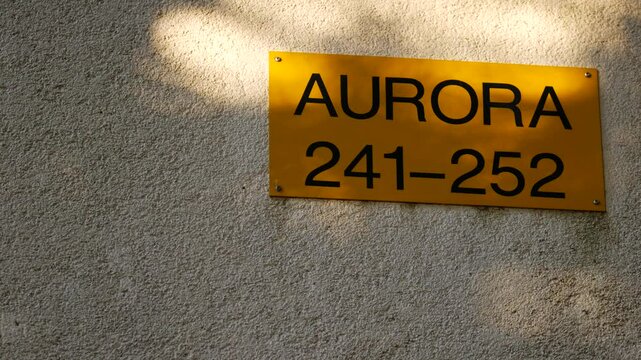 Golden plaque on plastered wall. Inscription Aurora and numbers 241-252. Apartment number in holiday camp. Gold hotel rooms sign. Background for subtitles or intro. Pula, Croatia - December 1, 2024