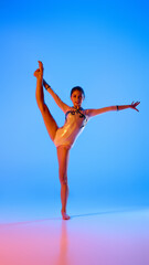 Fototapeta premium Strength and elegance,. Young gymnast balances gracefully, perfecting each move in pink neon light against gradient blue background. Concept of professional sport, active lifestyle, hobby. Ad