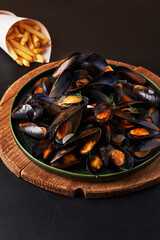 Delicious mussels served with crispy fries on wooden platter at a dining table