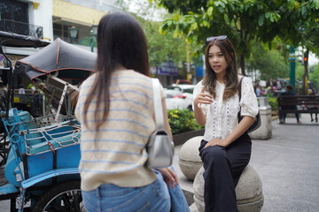 two asian women sitting on bech on the side of street
