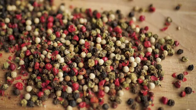 multi-colored allspice peas falling on a wooden cutting board in slow motion. Spices drop on the table. Spicy peppers add to meat and vegetables