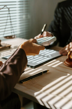 Businessman passing stack of money as bribe to lawyer signing contract in office, under table corruption and illegal deal concept
