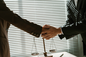 Two lawyers shaking hands in a law office with scales of justice in the foreground, symbolizing...