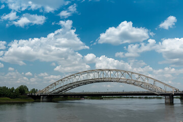 Naklejka premium A bridge over a river. A bridge with clouds and a river in the sky. Blue bridge in the nature with blue sky. Blue sky and clouds over the bridge in lifestyle nature.