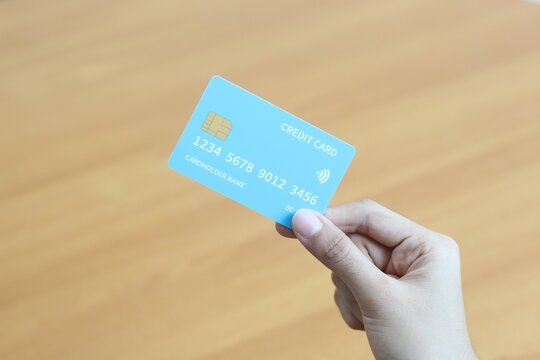 A Closeup Shot of a Person Holding a Light Blue Credit Card on a Wooden Surface: Secure Online Transactions and Financial Security