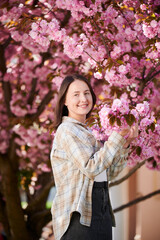 Woman allergic enjoying after treatment from seasonal allergy at spring. Portrait of happy beautiful woman smiling in front of blooming sakura tree at springtime. Spring allergy concept.