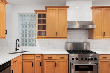 A kitchen with wood cabinets, a subway tile backsplash, black faucet, white marble countertop, and stainless steel appliances.