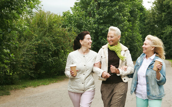 Three elderly ladies in casual clothes are walking in the park. Coffee and socializing, friendship in retirement.