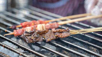 Beef meat on wooden skewer sticks are grilling on the metal grating with smoking from charcoal. Asian traditional streed food object, close-up.