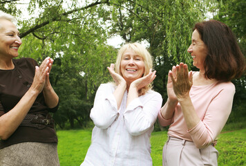 Obraz premium Women friends in the park celebrate a birthday. Clap your hands, congratulate, rejoice. Happy summer day.