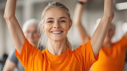 Personal trainner and training concept. Smiling woman in an orange shirt raising her arms during a fitness class, embodying joy and energy in a gym setting.