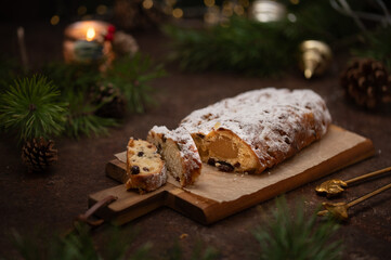Slices of German Christmas stollen cake on a wooden cutting board on rustic background with lights and decorations. Traditional handmade Christmas dessert. Fruit bread with nuts, raisins and marzipan.