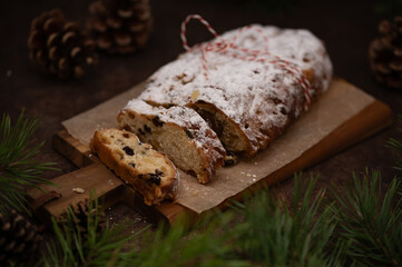 Slices of German Christmas stollen cake on a wooden cutting board on rustic background with lights and decorations. Traditional handmade Christmas dessert. Fruit bread with nuts, raisins and marzipan.