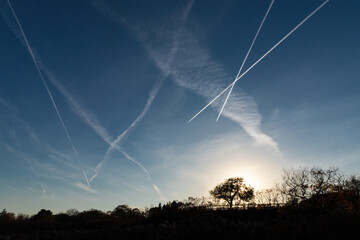 Sunrise or sunset with many numerous jet contrails showing air pollution and pollutants with sun...