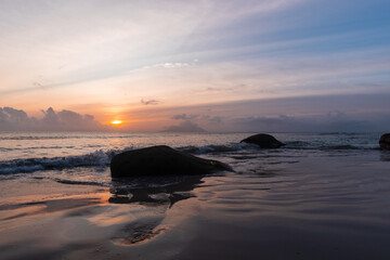 Naklejka premium Landscape with wet sand and silhouettes of dark coastal rocks