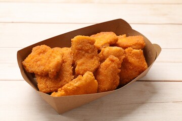 Tasty chicken nuggets in paper container on wooden table, closeup