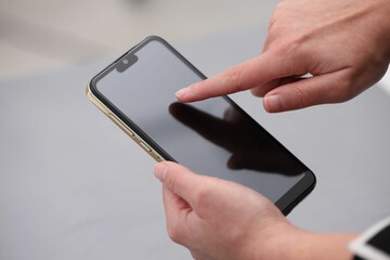 Woman using smartphone with blank screen on grey background, closeup