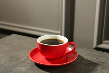 Red cup of aromatic coffee and saucer on dark textured table