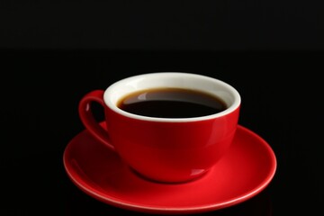 Red cup with coffee on black background, closeup