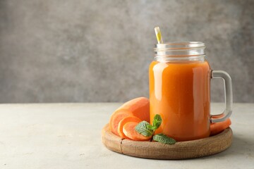 Fresh carrot juice in mason jar, vegetable and mint on gray textured table, space for text
