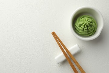 Hot wasabi paste in bowl and chopsticks on white table, top view. Space for text