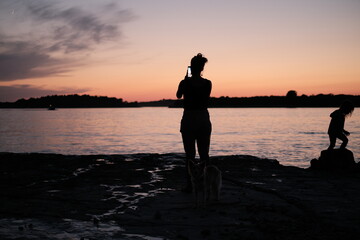Silhouette of young girl standing on the beach in Istria and taking photo of the sunset in the background.
