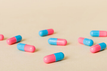 Heap of pink and blue pills on colored background. Tablets scattered on a table. Pile of red soft gelatin capsule. Vitamins and dietary supplements concept