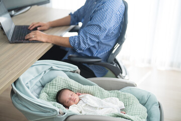 赤ちゃんの育児をしながら自宅でテレワークの仕事をする父親