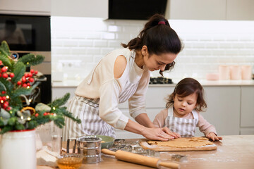 Happy family mother and little child daughter cutting cookies of raw gingerbread dough in kitchen. Christmas time