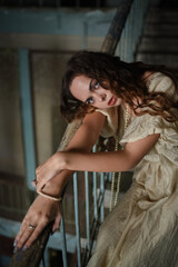 Obraz premium Beautiful young woman in a beige long dress posing on stairs of an old building..