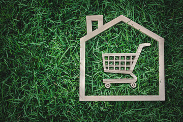 E-commerce and Sustainability: Wooden House Frame with Shopping Cart on Green Grass