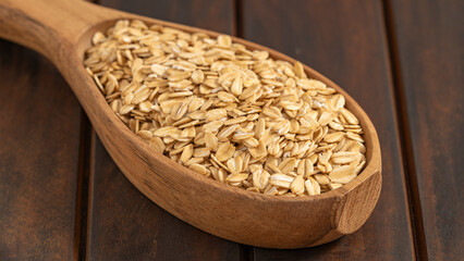 Rolled oats in a wooden scoop on a dark rustic wooden surface. Perfect for themes of healthy eating and natural lifestyle.