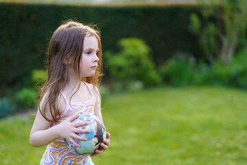 Obraz premium Little sad lightly dressed wet girl playing with ball in backyard in summer. Concept of cheerful active child