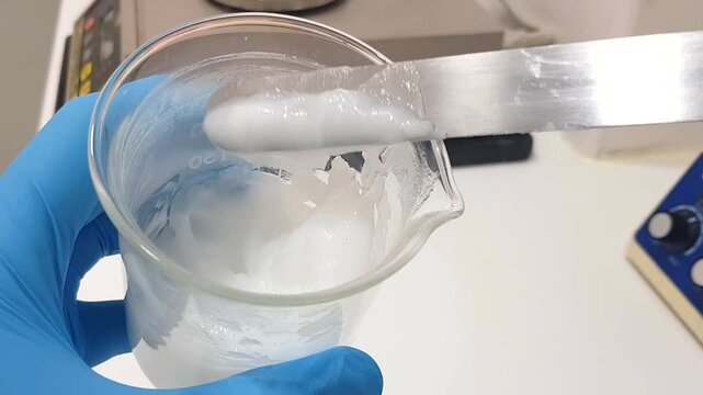 Close-up footage of a beaker containing a white emulsion being stirred with a spatula. The creamy substance is mixed thoroughly, showcasing laboratory precision in formulation processes. Ideal for sci