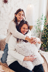 Mother hugging her daughter by decorated Christmas tree at home. Holiday interior. Happy family posing in studio