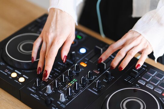 Close-up of a person&rsquo;s hands with red painted nails adjusting knobs and sliders on a DJ controller