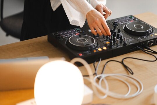 Close-up of a person&rsquo;s hands with red painted nails adjusting knobs and sliders on a DJ controller