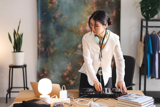 A focused DJ wearing headphones uses a DJ controller, blending music tracks in a well-lit studio environment with modern equipment on a wooden desk