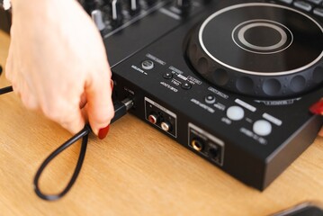 Close-up of a hand with red nails connecting a cable to a DJ controller