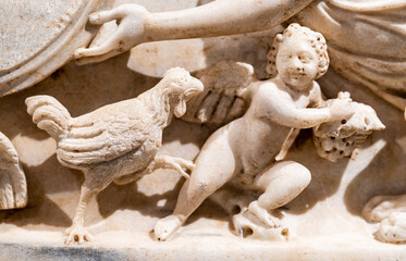Close-up on sculptures carved in a marble wall representing a chicken interacting with a cupid