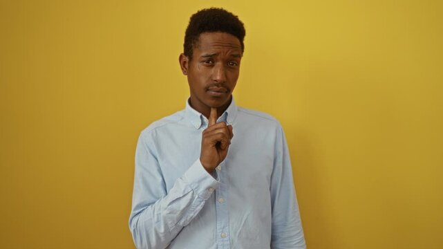 Young african american man wearing shirt standing thinking with chin on finger, looking up in doubt wondering concentrated over isolated yellow background