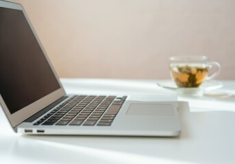 Fototapeta premium Modern workspace showing laptop computer and herbal tea infusion on white desk, ideal for remote work and freelance lifestyle