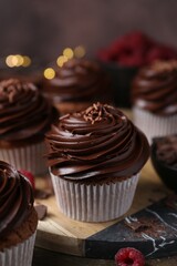 Tasty cupcakes with chocolate cream and raspberries on wooden table, closeup